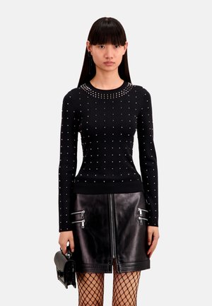 Maglione nero con decorazioni a borchie, design aderente, maniche lunghe, abbinato a una gonna in pelle nera con cerniere argentate e collant in rete.