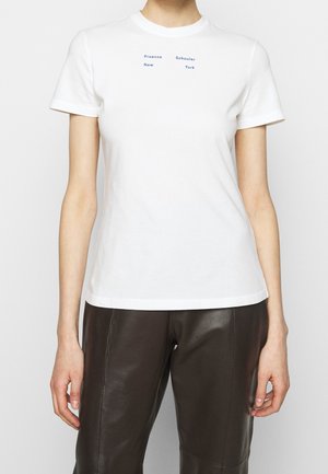 T-shirt blanc ajusté à manches courtes avec petit texte bleu « Proenza Schouler New York » sur la poitrine, porté avec un pantalon en cuir noir.