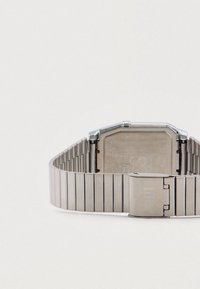 Ασημένιο μεταλλικό ρολόι χειρός με οκταγωνική κάσα και μπρασελέ από συνδεδεμένους κρίκους. Διαθέτει ματ φινίρισμα και κούμπωμα κλεισίματος, παρουσιάζοντας έναν μινιμαλιστικό σχεδιασμό.