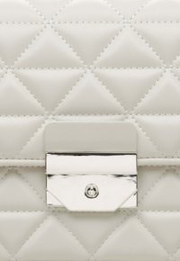 Prošívaná bílá kožená kabelka s diamantovým vzorem, stříbrným zapínáním na klip a horizontálním popruhem; hladký povrch s kontrastním prošitím.