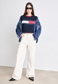 Marineblå beskåret t-shirt med røde og hvide striber, parret med en denimjakke, hvide vide bukser og sorte hælede sko med spidse tæer.
