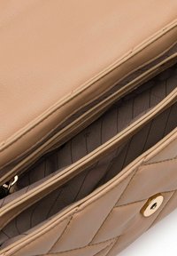Interior de un bolso de mano de cuero beige con dos compartimentos, acentos en hardware dorado y una textura acolchada en el exterior. Forro con finas rayas.