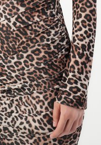 Close-up of a hand resting on a ruched leopard print dress sleeve and hip area with brown, black, and beige spots.