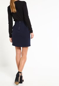 Mörkblå texturerad kjol med dragkedja bak, tillsammans med en tajt svart långärmad topp och svarta sandaler med remmar.