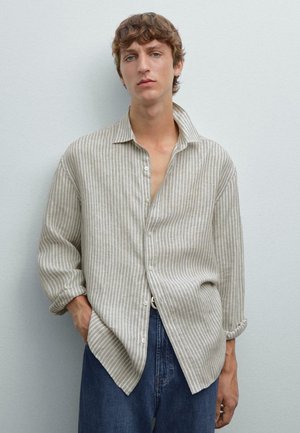 Chemise en lin beige clair avec des rayures blanches verticales, un col et une fermeture à boutons. Manches ajustées retroussées au niveau des poignets. Jean en denim foncé.