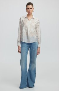 Witte, lichte blouse met subtiele geborduurde patronen, gecombineerd met lichtblauwe flared jeans en een kraagontwerp.