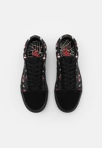 Baskets noires avec un bout en daim texturé, présentant un motif graphique de dents rouges et un design en toile sur les côtés en tissu et les semelles intérieures.