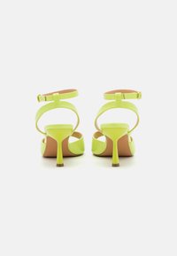Pair of neon yellow high-heeled sandals with ankle straps and gold buckles, shown from the back on a white background.