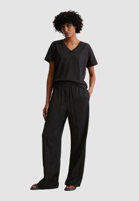 Zwarte V-hals T-shirt gecombineerd met losse zwarte broeken. De outfit heeft een zachte textuur en een relaxte pasvorm, met een elastische taille en zijzakken.