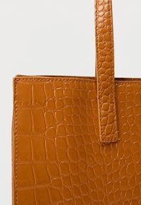 Bruine tote bag met krokodillenprint, voorzien van een gestructureerde vorm, een gladde textuur en een platte handgreep om te dragen.