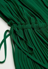 Tissu vert plissé avec une taille froncée et un détail de lien, présentant une texture lisse et un design fluide.