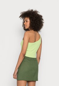 Top verde assimétrico feito de tecido canelado, combinado com uma saia verde xadrez ajustada, destacando a suavidade do tecido e o design ajustado.