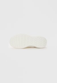 Semelle de chaussure en caoutchouc blanc avec un motif texturé, présentant un design ondulé et des bords surélevés pour la prise. Forme plate et arrondie.