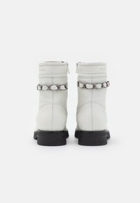 Bottes de cheville en cuir blanc avec une semelle noire, ornées d'un détail en chaîne autour du col et d'une fermeture éclair à l'arrière.