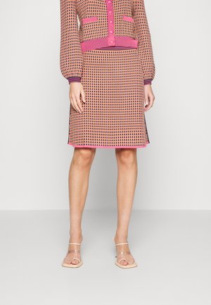Ensemble en tricot composé d'un haut à motifs et d'une jupe en rose et beige, avec des accents côtelés et une silhouette droite. Sandales transparentes.