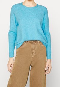 Light blue crew-neck sweater with ribbed cuffs and hem, made from soft material. Paired with high-waisted brown pants featuring front pockets.