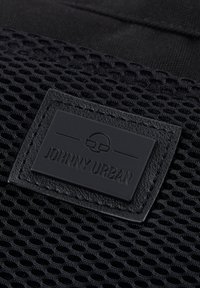 Fekete hálós anyag texturált felülettel, egy téglalap alakú bőr címkével, amelyen nagybetűs felirattal olvasható a "JOHNNY URBAN".