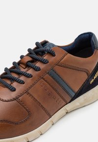 Scarpa in pelle marrone con accenti blu navy, punta tonda, tomaia texturizzata e lacci scuri. Presenta un logo e una suola in gomma chiara.