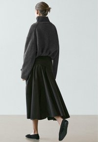 Oversized gebreide trui in donkergrijs met een hoge kraag, gecombineerd met een vloeiende zwarte rok en zwarte instapschoenen. Gestructureerde stof, casual ontwerp.