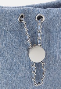 Jasnoniebieska torba z denimu z pikowanym wzorem, wyposażona w srebrne metalowe oczka oraz łańcuszek na górze, z okrągłym metalowym zamknięciem.