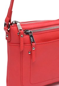 Červená kožená crossbody taška s dvojitými zipsovými priehradkami, striebornými kovovými doplnkami a hladkou textúrou. Detaily tvoria látkové popruhy.