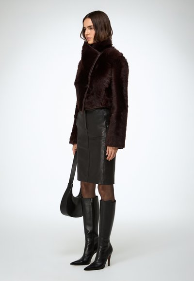 Giacca corta in ecopelliccia bordeaux con collo alto, gonna a tubino in pelle nera e stivali neri in pelle con tacco a spillo al ginocchio, abbinati a una borsa nera.