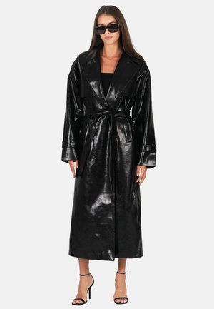 Cappotto trench in ecopelle nera con ampio colletto, vita con cinturino e maniche lunghe. Texture liscia e lucida con silhouette di lunghezza media.