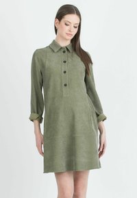 Abito verde oliva con colletto, chiusura a bottoni frontale, maniche tre quarti arrotolate ai polsini, tessuto testurizzato e tasche laterali.
