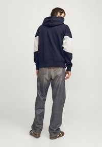 Sudadera azul marino con mangas blancas, fabricada en suave algodón, de corte relajado, combinada con jeans de denim holgados y sandalias marrones. Diseño minimalista.