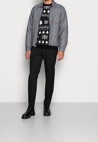 Grå rutig jacka med röda accenter, svart mönstrad tröja med snöflingor och träd, svarta byxor och svarta ankelskor.