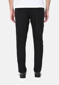 Pantaloni cargo neri con una vestibilità slim, dotati di tasche laterali, polsini elastici alla caviglia e un tessuto testurizzato. Indossati con scarpe nere.