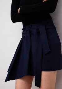 Marinblå omslagskjol i ett smidigt tyg, med hög midja, plisserad design och ett brett bälte med långa band. Snabbtorkande material.