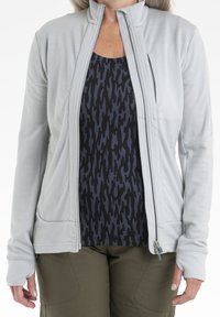 Ljusgrå zip-up-jacka med hög krage, med en mjuk textur, sidofickor och tumhål; bärdes över en svart och grå mönstrad topp.