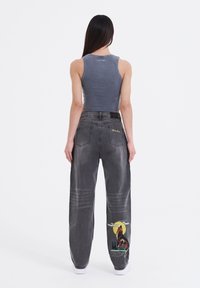 Gray cropped tank top and loose-fit gray jeans with animal graphic on the right leg, featuring a yellow moon and trees.