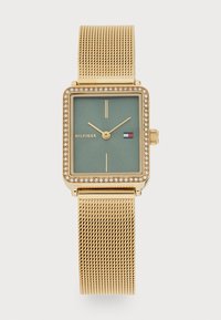 Montre rectangulaire dorée avec un cadran vert, accents en cristal, bracelet en maille dorée et index horaires minimalistes. Le logo de la marque est présent.