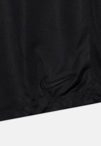 Mustaa kangasta, jossa on ommeltu Nike-swoosh-logo helmassa, näyttäen hienovaraisen tekstuurin ja kaksinkertaisen ompeleen saumassa.