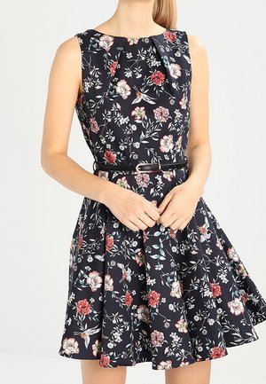 Sleeveless navy dress with red, white, and pink floral and bird print, fitted waist with thin black belt, and flared skirt.