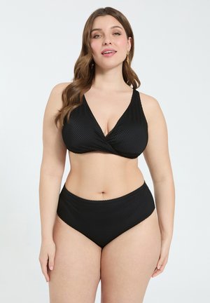 Kurvige Frau mit einem strukturierten schwarzen Bikini mit hoch tailliertem Unterteil, stehend vor einem einfarbigen hellen Hintergrund.