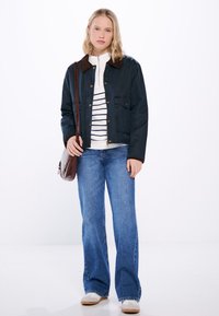 Marinblå bomullsjacka med brun krage, vit randig skjorta under, blå denim med vida ben, och beige sneakers, accessoriserad med en brun väska.