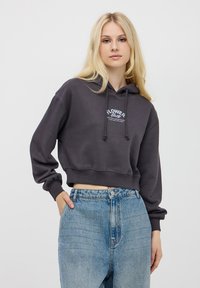 Przycięta, ciemnoszara bluza z kapturem z sznurkami i grafiką z przodu. Połączona z jasnoniebieskimi dżinsami z wysokim stanem. Gładka faktura.