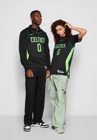 Svart og grønt Nike Celtics-drakter med nummer 0, båret over svarte og lysegrønne antrekk. Tekstur: mesh. Innstilling: nøytral bakgrunn.
