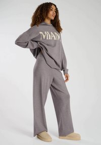 Grauer oversized Hoodie mit "MIAMI"-Schriftzug, kombiniert mit passenden weit geschnittenen Hosen. Weiche Textur, lockere Passform und lässiges Design. Unauffällige beige Schuhe.