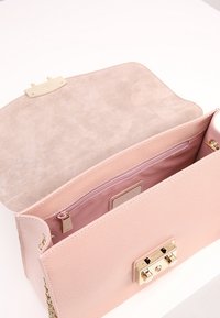 Růžová kožená kabelka s texturovaným povrchem, zlatým kováním na klapce, podšívkou a prostornou kapsou se zipem. Pohled na otevřený design.