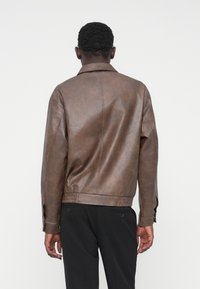 Veste marron en simili cuir avec un col classique, un ourlet côtelé et des poignets à boutons. Texture lisse et design simple sans ornements.