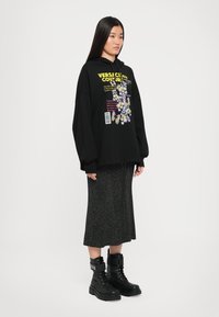 Sweatshirt preto oversized com gráficos florais e texto, combinado com uma saia cinza até ao joelho e botas de combate pretas com atacadores.