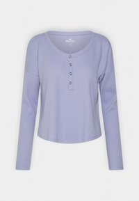 Ljuslila långärmad topp med ribbat mönster, V-ringning och tre dekorrande knappar vid bröstet. Avslappnad, ledig passform.