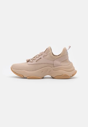 Beżowy sneaker z dzianiny z grubą podeszwą, sznurowany z przodu, z pętlą z tyłu, pokazany z profilu na białym tle.