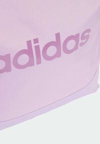 Világoslila szövet táska, amelyen egy nagy, enyhén sötétebb lila "adidas" logó található. Puha tapintás, sima felület és kerekített szélek jellemzik.