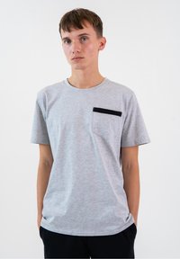 Szary krótki t-shirt z miękkiego materiału, z czarną kieszenią na lewej piersi, okrągłym dekoltem i luźnym krojem.