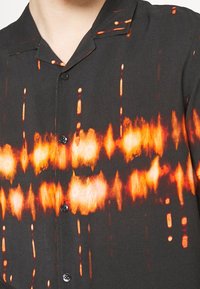 Kortärmelig shirt van lichtgewicht stof, met een zwarte basis en een abstract patroon in oranje en geel, en zwarte knopen.